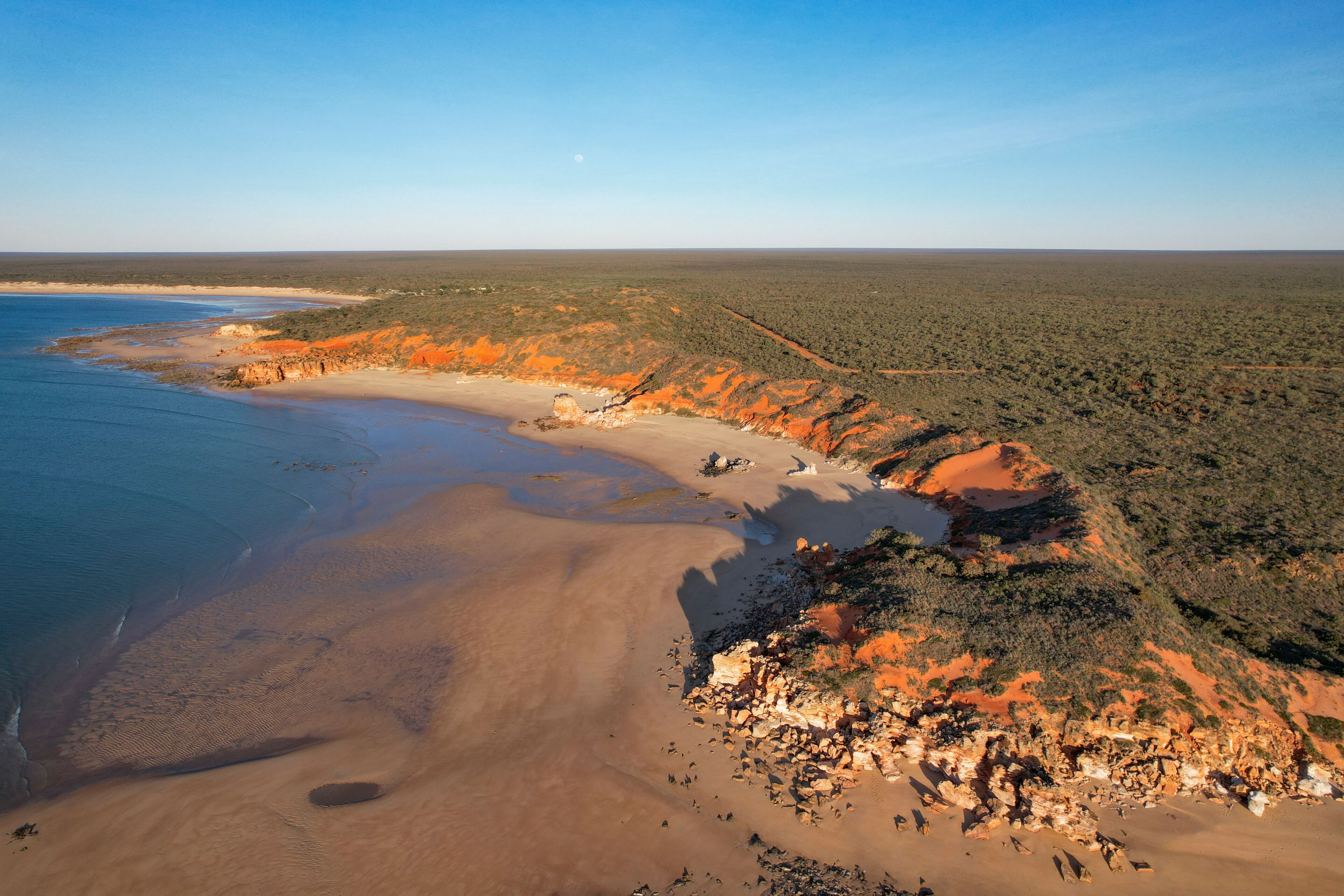 Aerial view of echo beach resort coastline with ochre cliff and the moon, Lagrange, Western Australia.