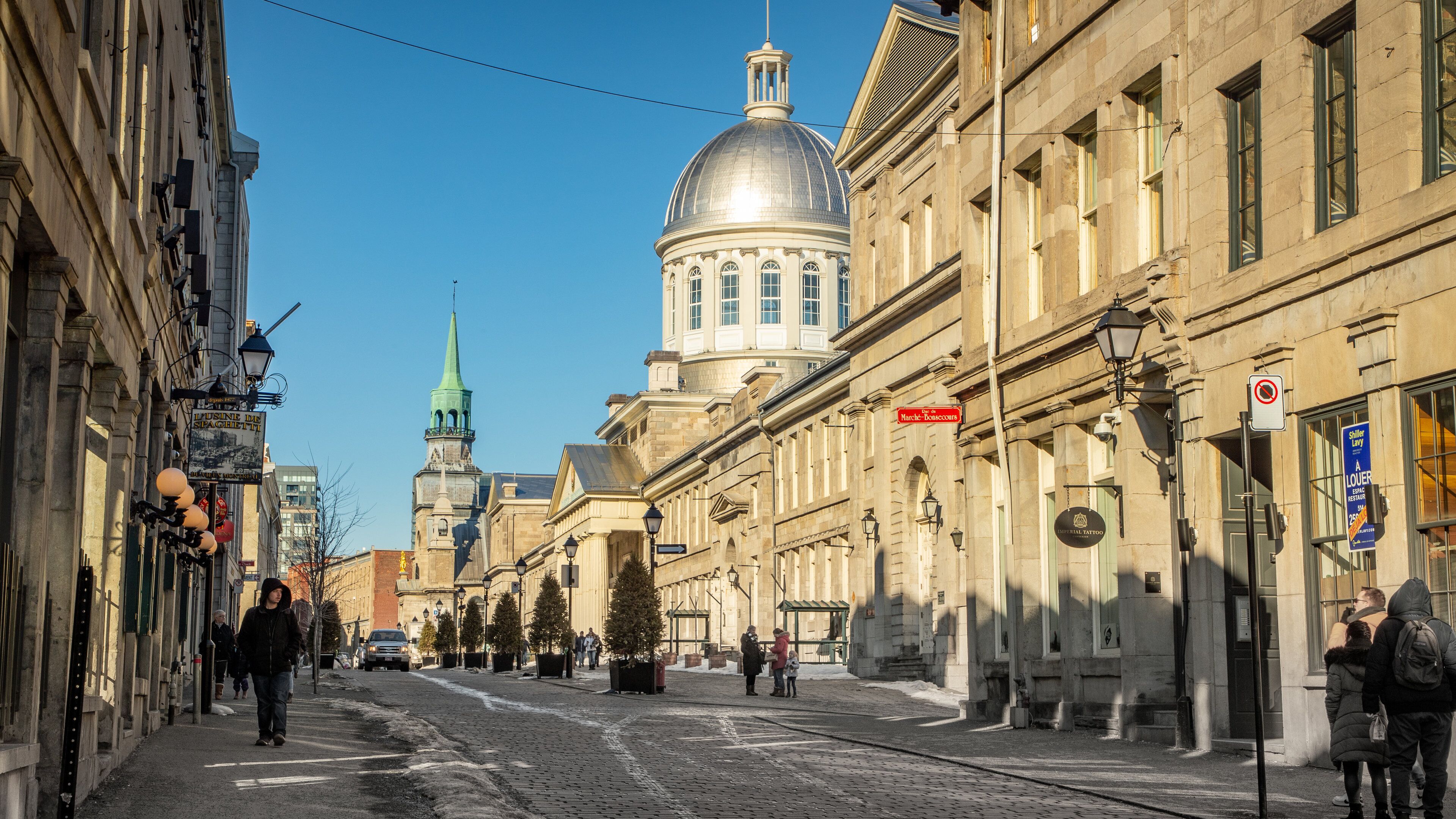 Una calle empedrada flanqueada por edificios históricos, una cúpula destacada y una aguja de iglesia.