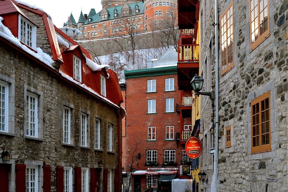A snow-covered cobblestone street with historic buildings, a prominent tower, and a sign for "Château de la Citadelle."