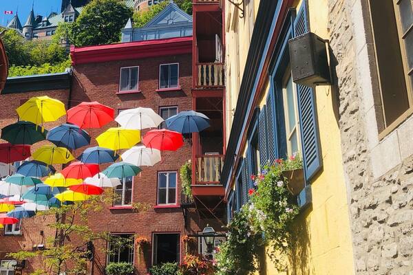 Une rue animée, parée de parasols colorés, un bâtiment sur lequel on peut lire l’inscription « Le Sach », et un château en arrière-plan.