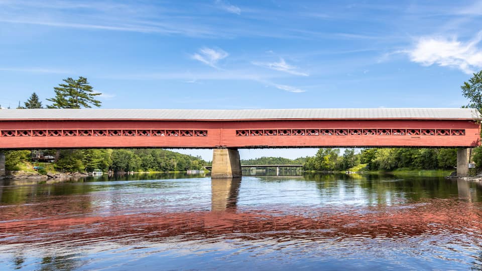 A red covered bridge spanning a river with a clear sky above.