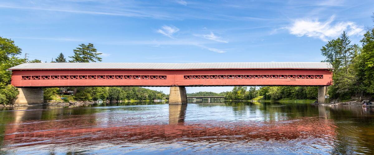 A red covered bridge spanning a river with a clear sky above.