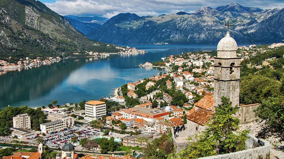 A coastal town with a prominent tower, a lake, and mountainous terrain in the background.
