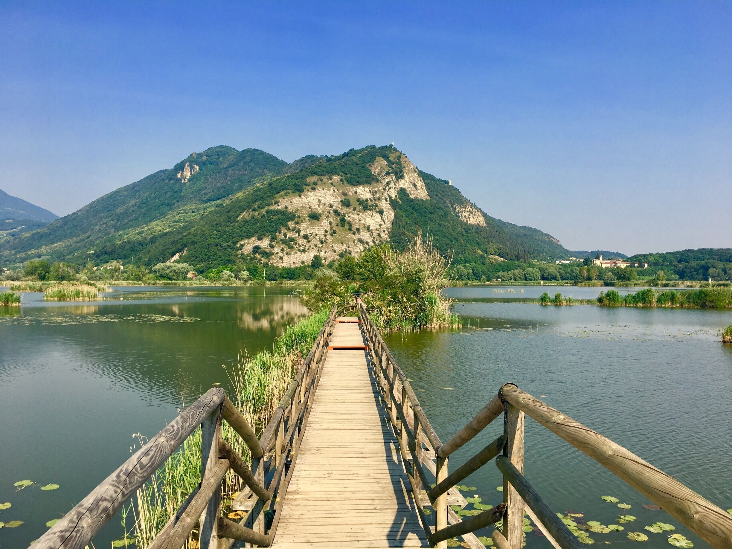 A wooden bridge over a calm river with mountains in the background.