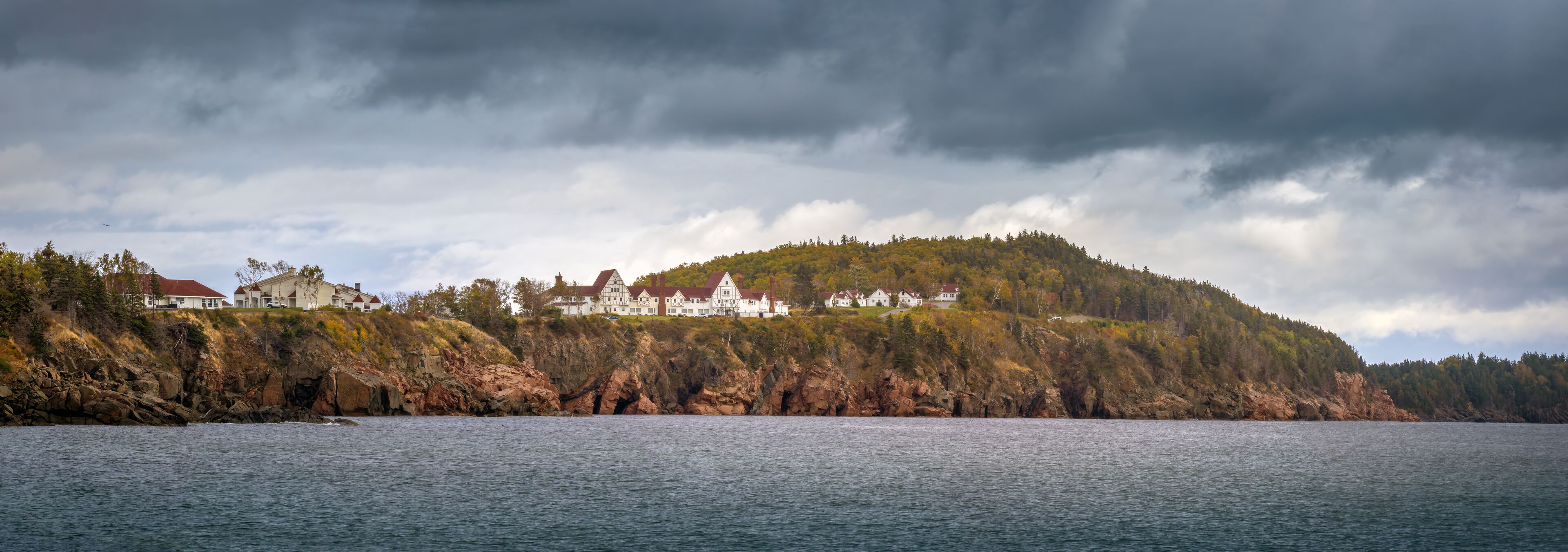A coastal landscape with a large estate on a hill, surrounded by water and dense forest.