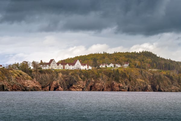 A coastal landscape with a large estate on a hill, surrounded by water and dense forest.