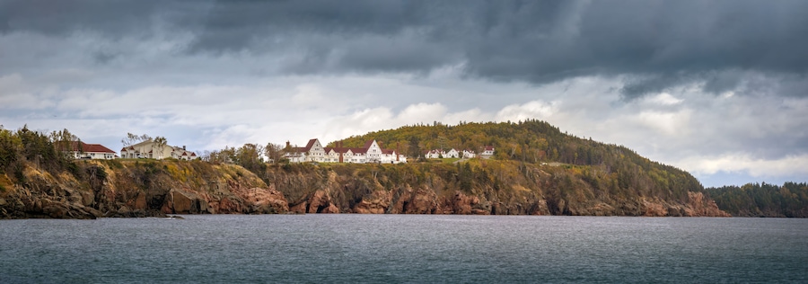 A coastal landscape with a large estate on a hill, surrounded by water and dense forest.