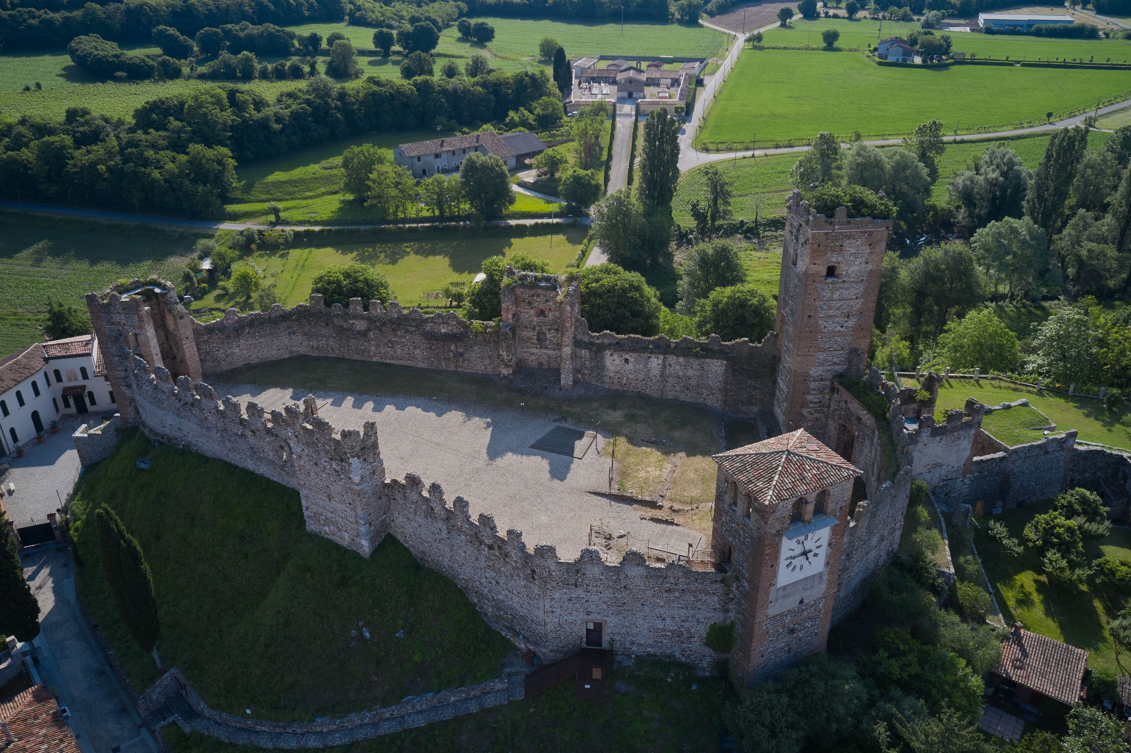 An aerial view of a medieval castle with a moat, surrounded by lush green fields and a river.