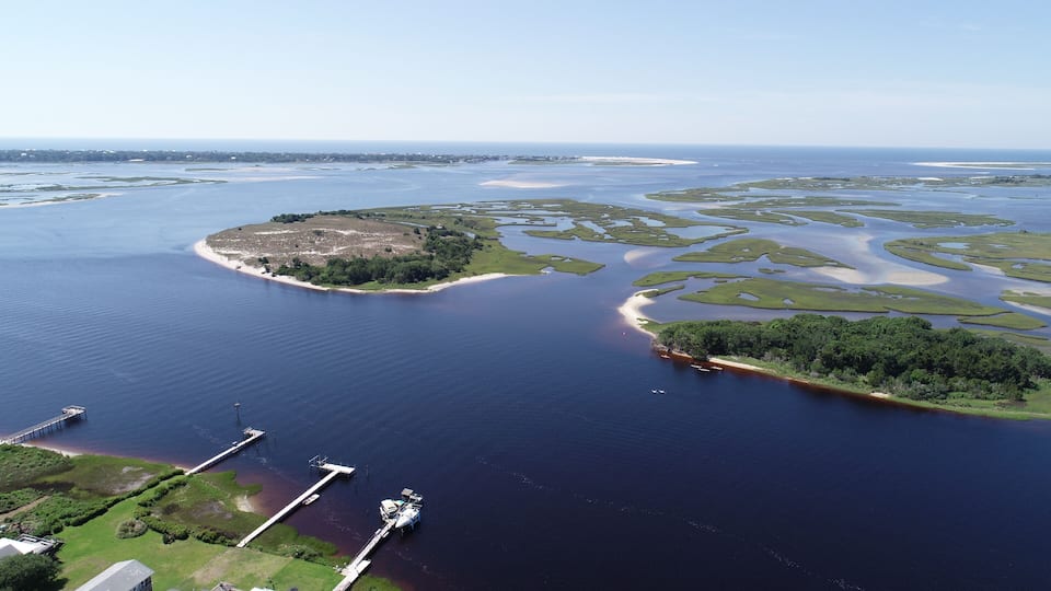 A coastal landscape with a large body of water, a small island with dense vegetation, and a pier with boats.