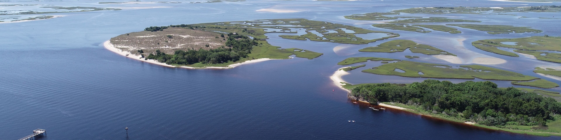 Un paisaje costero con una extensa masa de agua, una pequeña isla de vegetación densa y un muelle con barcos.