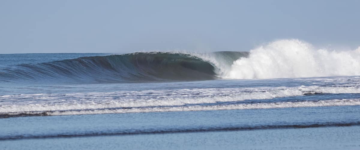A large ocean wave with white foam at the crest, indicating strong surf conditions.