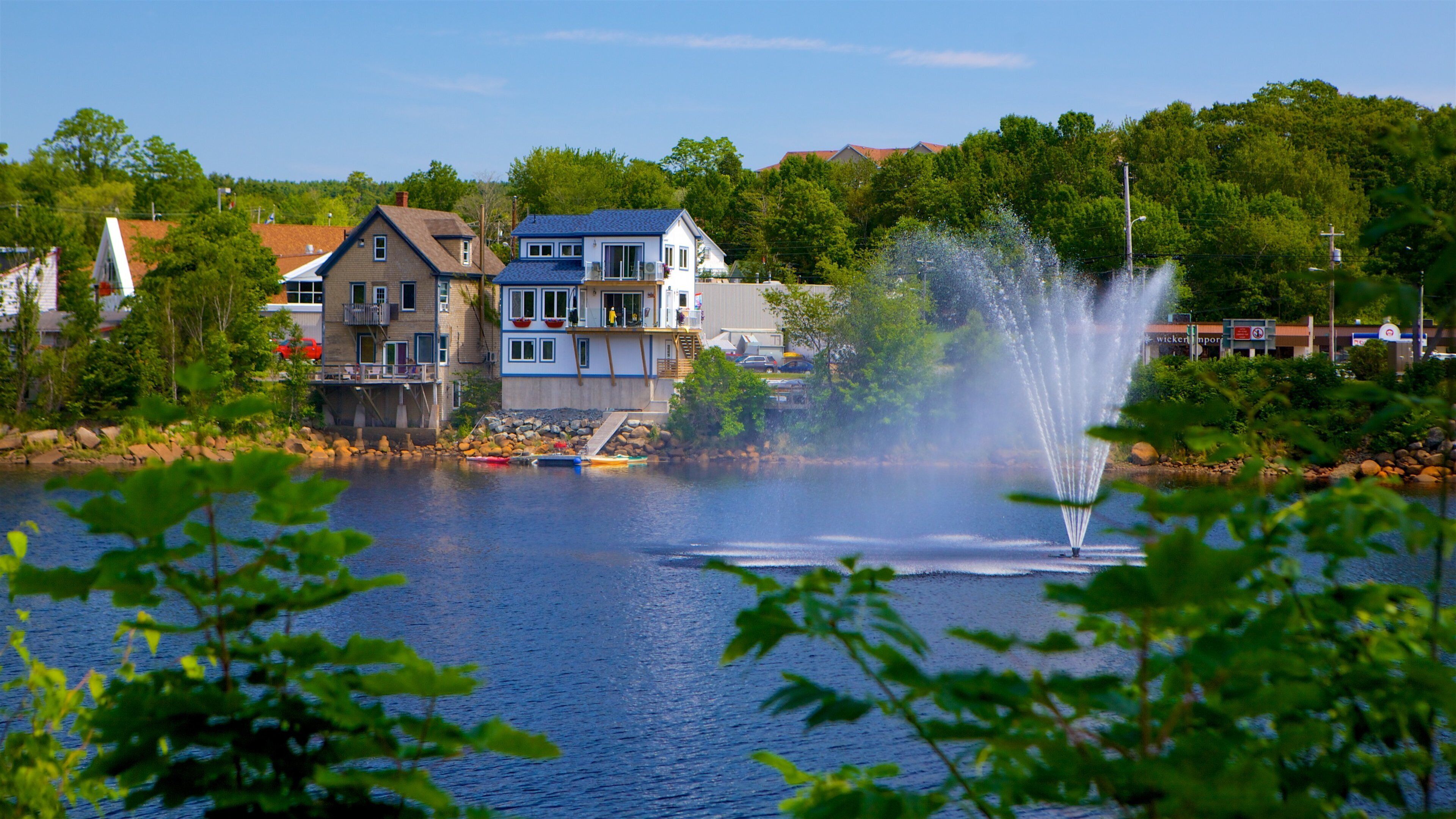 A lake with a fountain, houses, and trees.
