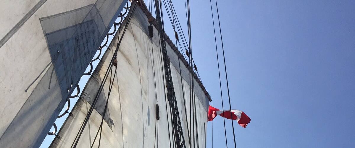 A close-up of a sailboat's mast with rigging and a red and white flag.