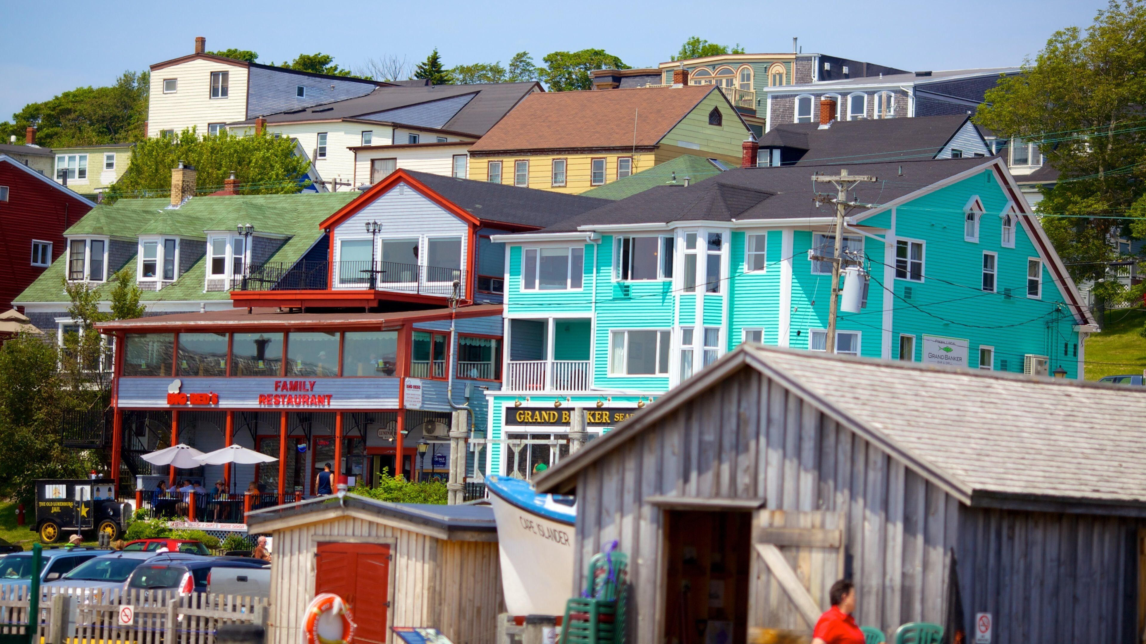 A colorful waterfront town with a family restaurant, a Grand Baker Seafood restaurant, and a dock with a boat named Cape Islander.
