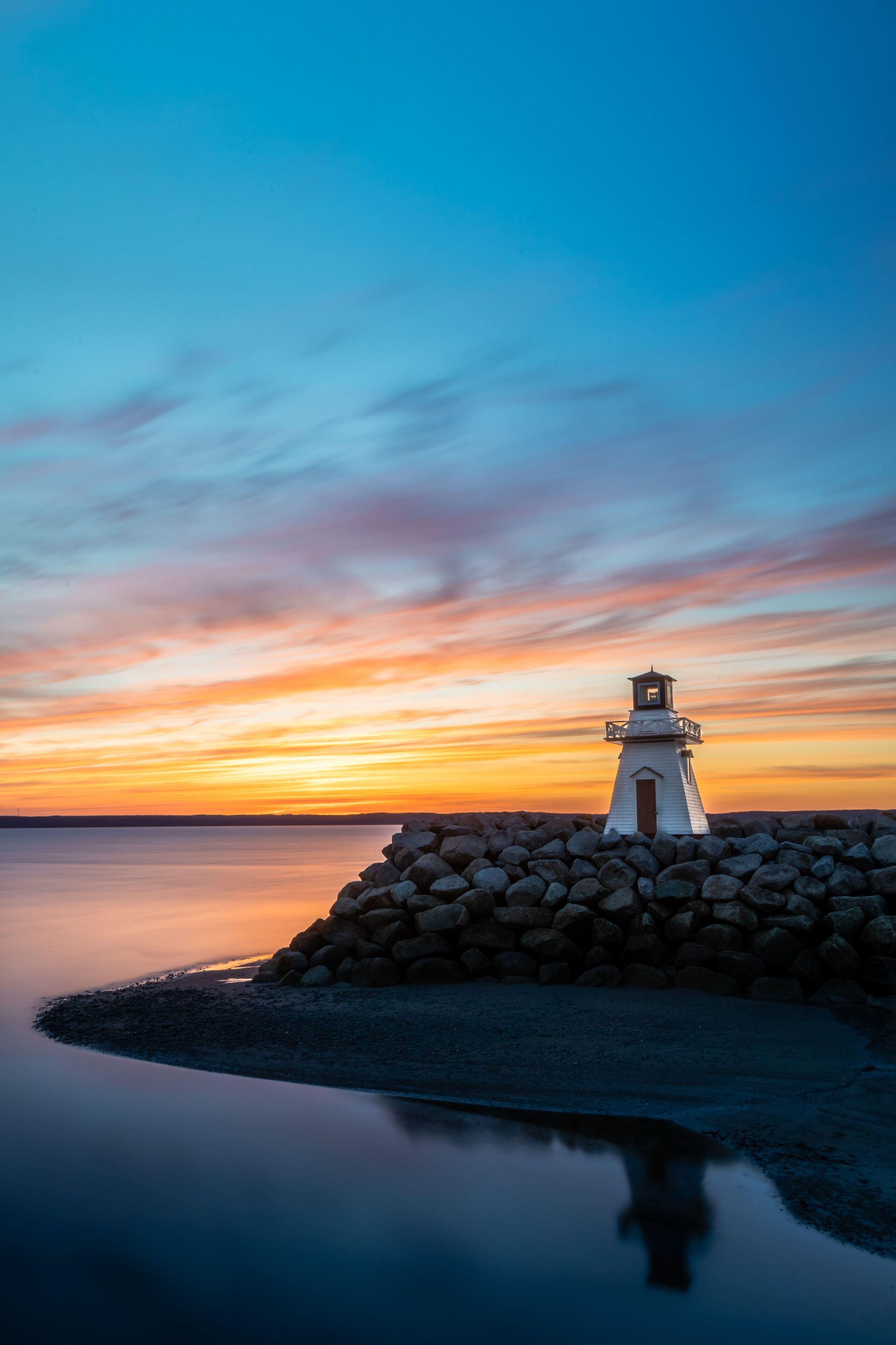 Um farol sobre um afloramento rochoso, com o pôr do sol ao fundo.