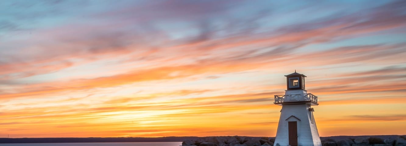 Um farol sobre um afloramento rochoso, com o pôr do sol ao fundo.