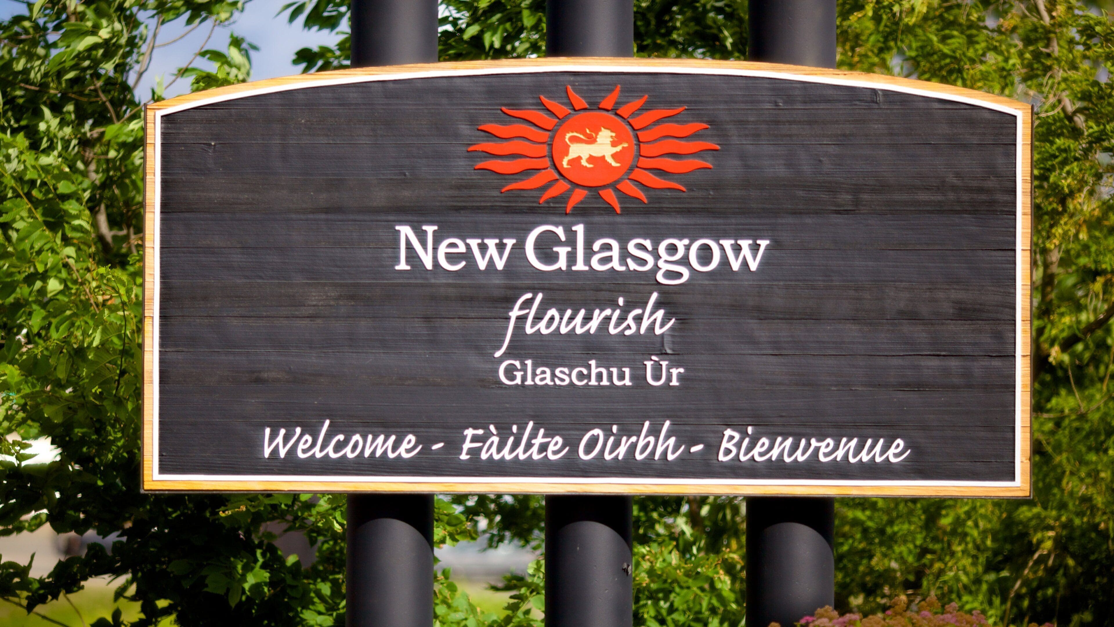 A welcome sign for New Glasgow with a sun and lion emblem, and text in English, German, and French.