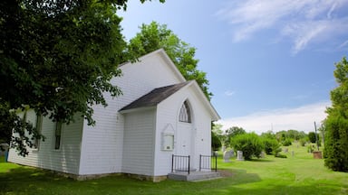 Une église blanche, dotée d’un clocher, entourée d’un cimetière où se dressent des pierres tombales.