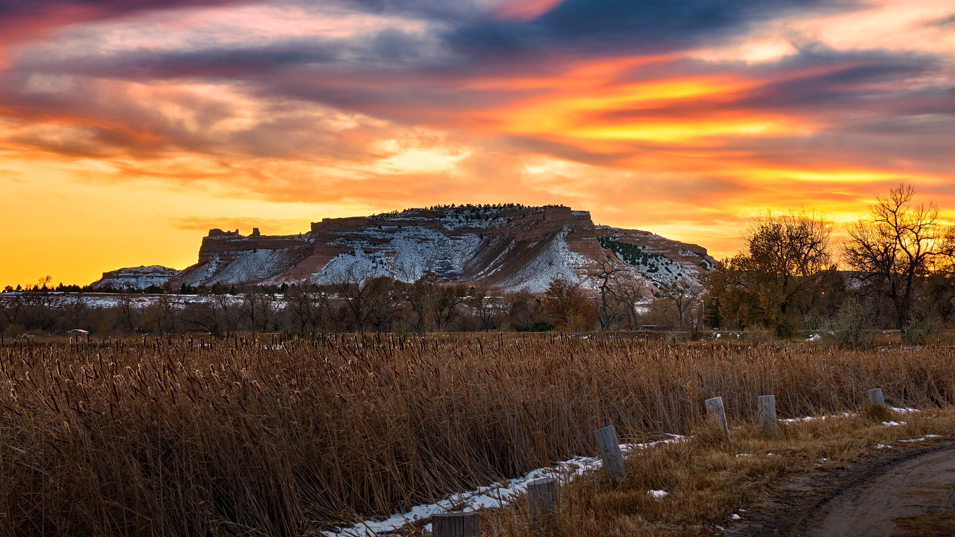 A snow-covered hill with a sunset sky and a dirt path in the foreground.
