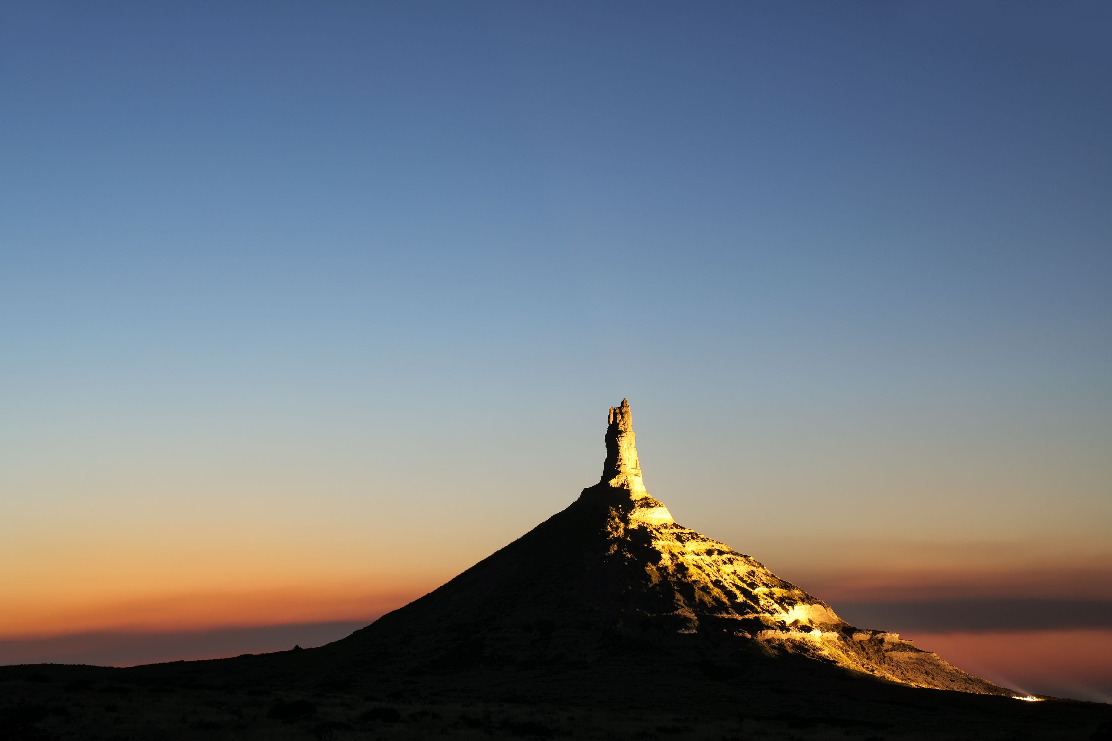 A mountain peak with a distinct conical shape, illuminated by the setting or rising sun.