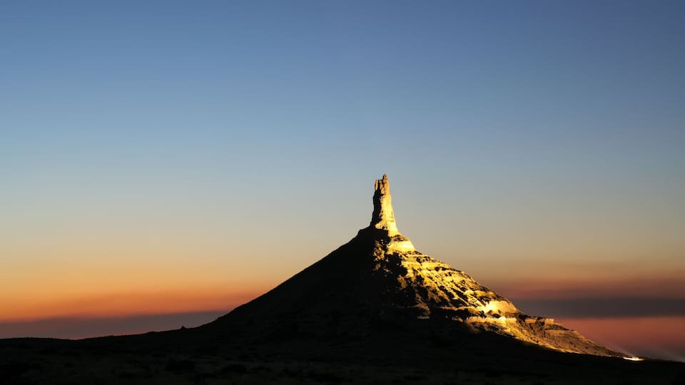 A mountain peak with a distinct conical shape, illuminated by the setting or rising sun.
