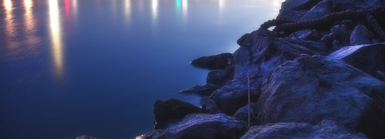 Un pont au crépuscule, dont les lumières se reflètent sur l’eau.