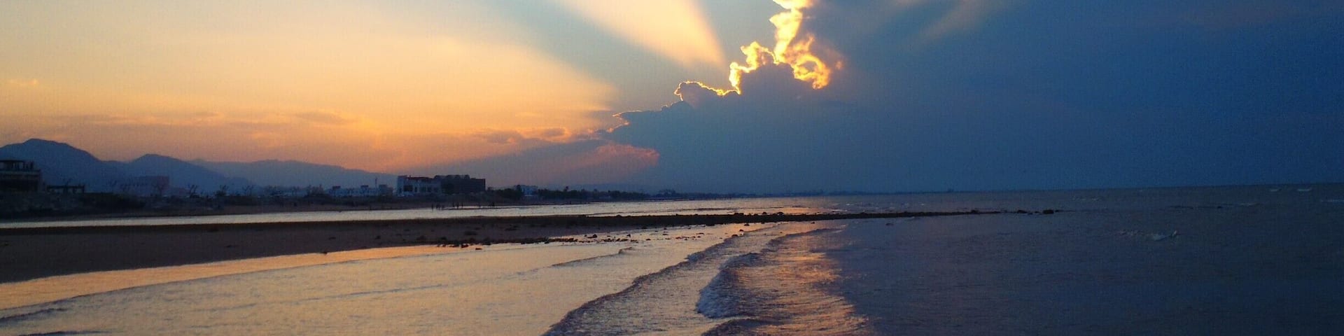 A beach at sunset with sunlight streaming through clouds.