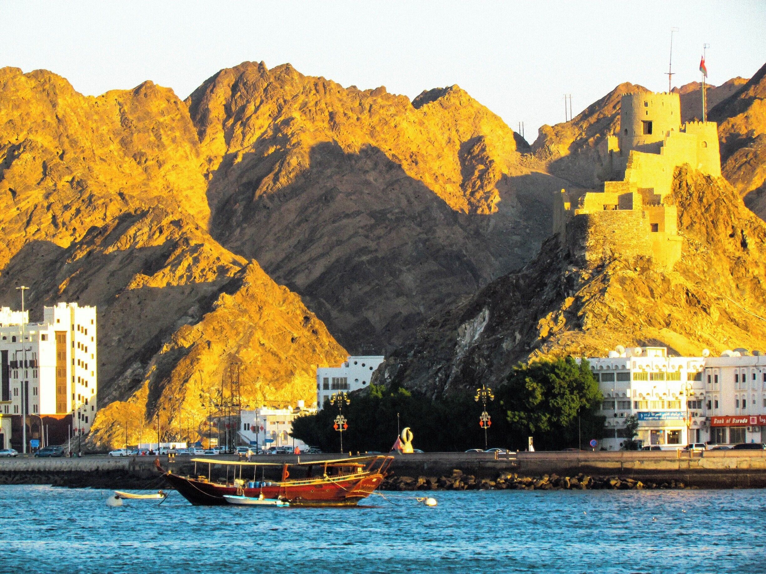 Un pueblo costero con un castillo imponente en una colina, barcos en el agua y edificios a lo largo de la orilla.