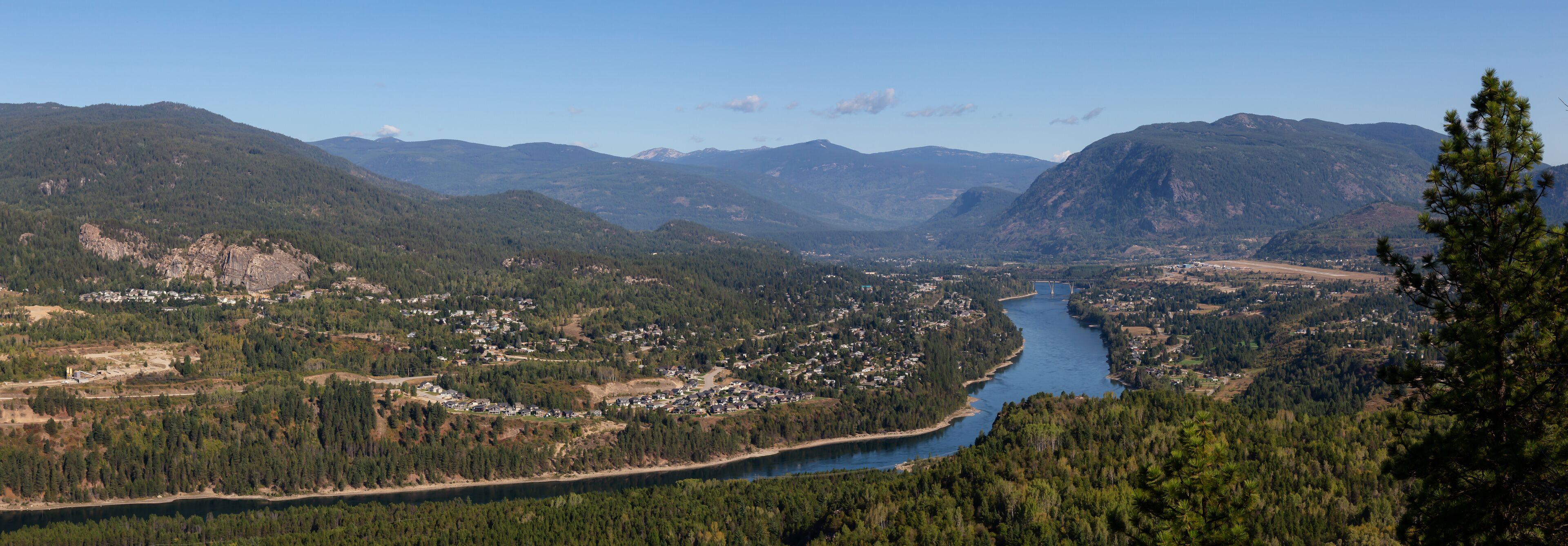 A river winding through a valley surrounded by mountains, with a bridge crossing the river and a town along the riverbank.