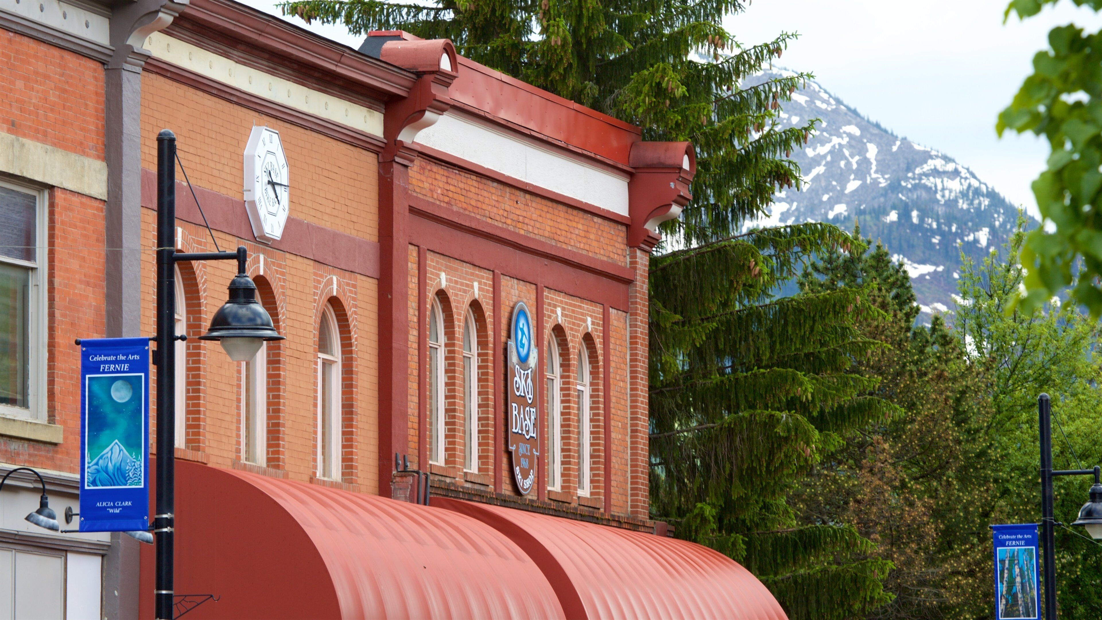 A brick building with a clock, a red awning, and a mountain in the background.