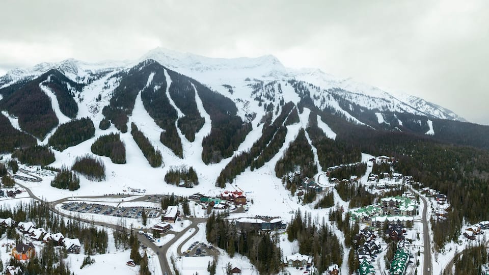 A snow-covered mountain range with ski trails and a resort area.