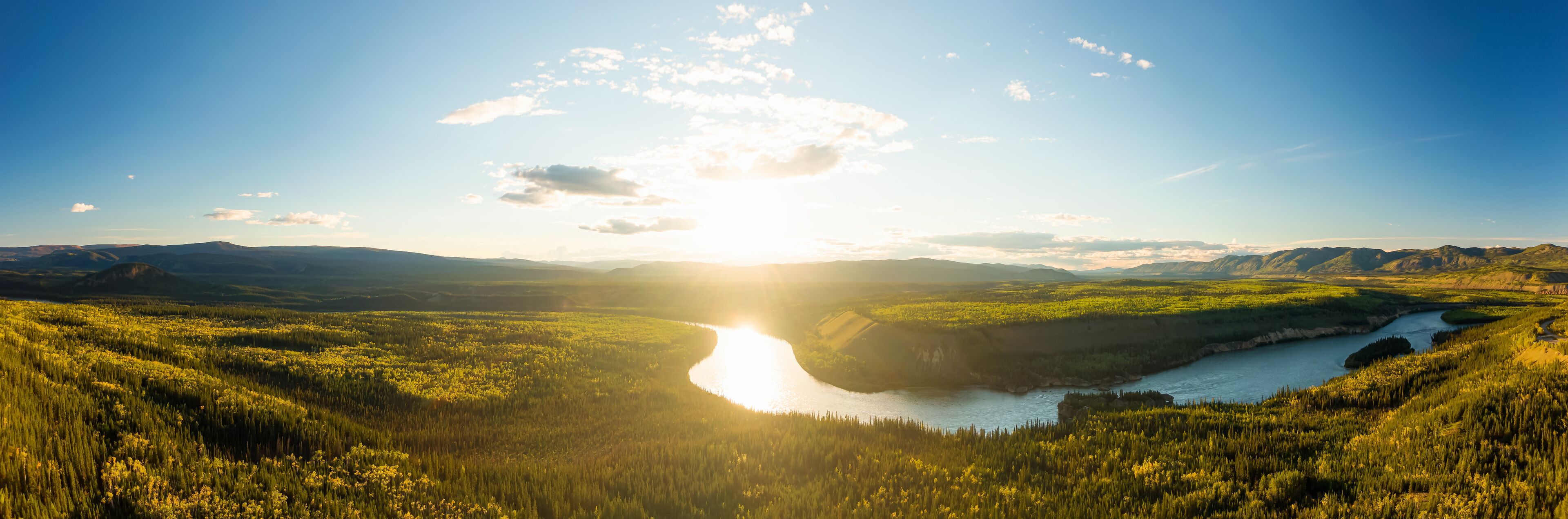 Beautiful View of Scenic Valley from Above alongside Winding River, Forest and Mountains at Sunset. Aerial Drone Shot. Taken near Klondike Highway, Yukon, Canada.