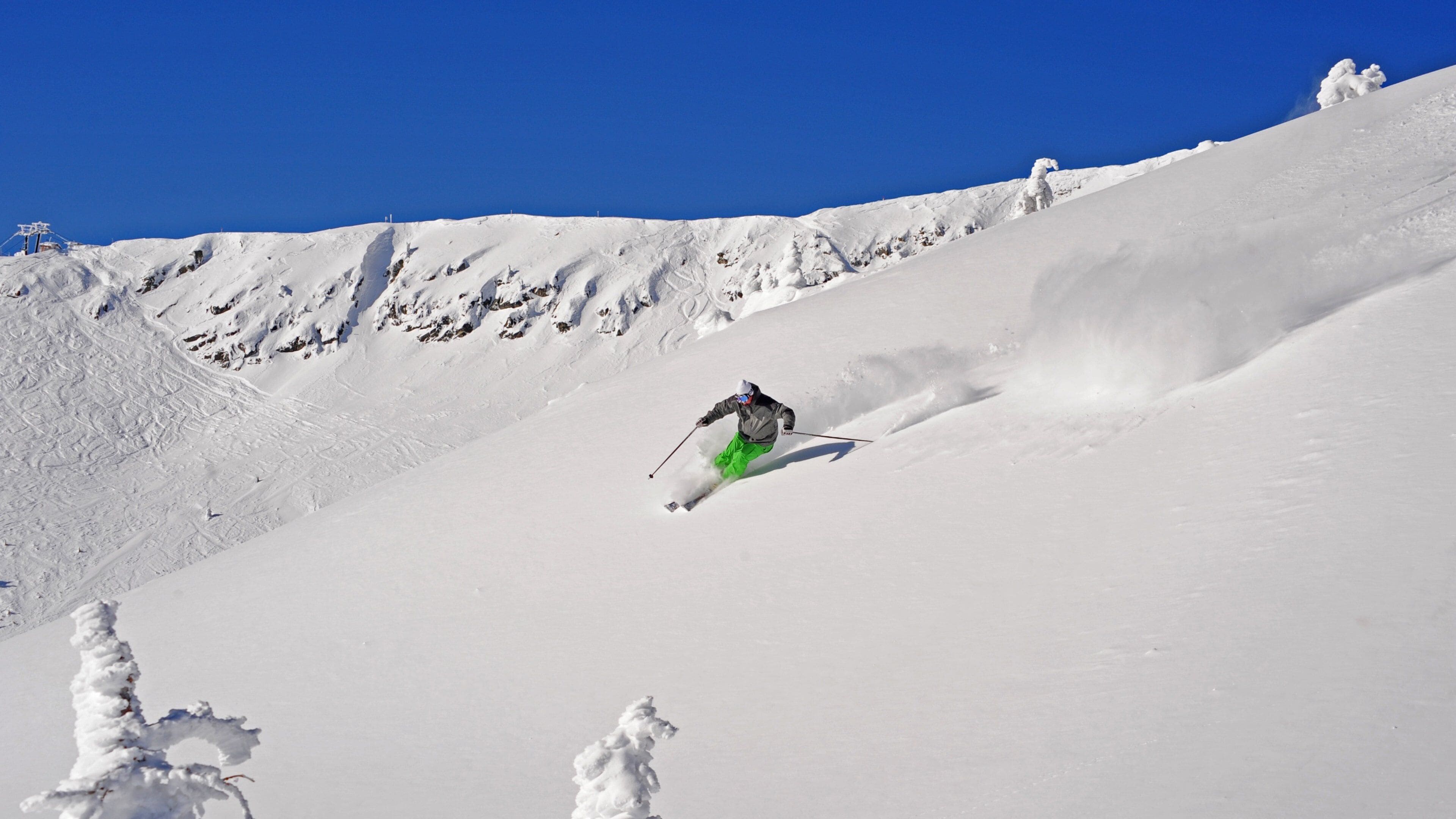 A skier descending a snow-covered slope with a clear blue sky.
