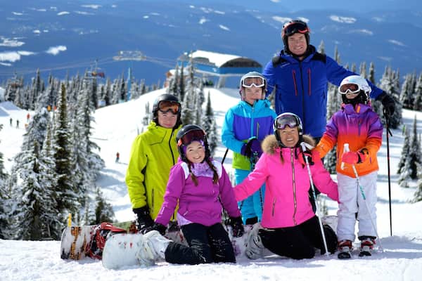 A group of people on a snowy mountain with ski lifts and snow-covered trees in the background.