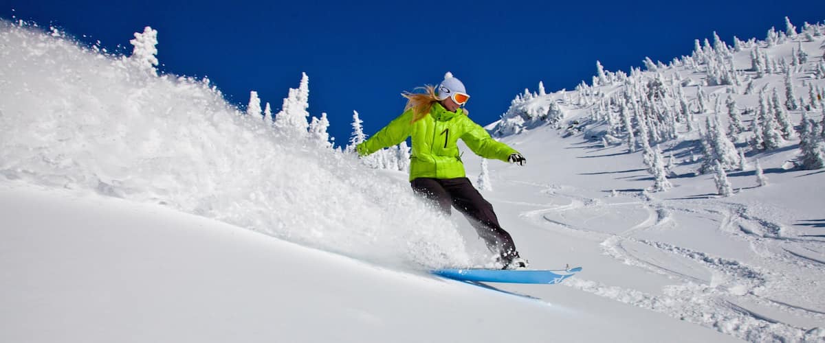 A person snowboarding down a snowy slope with trees in the background.