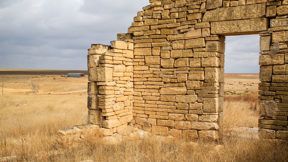 A stone ruin with a window, surrounded by dry grass and a flat landscape.