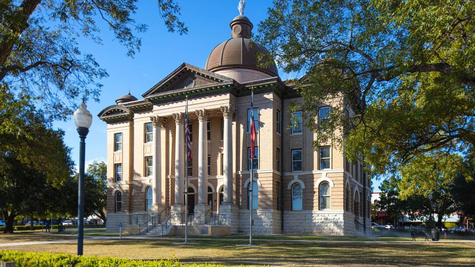 A historic building with a dome and columns, surrounded by trees and a well-maintained lawn.