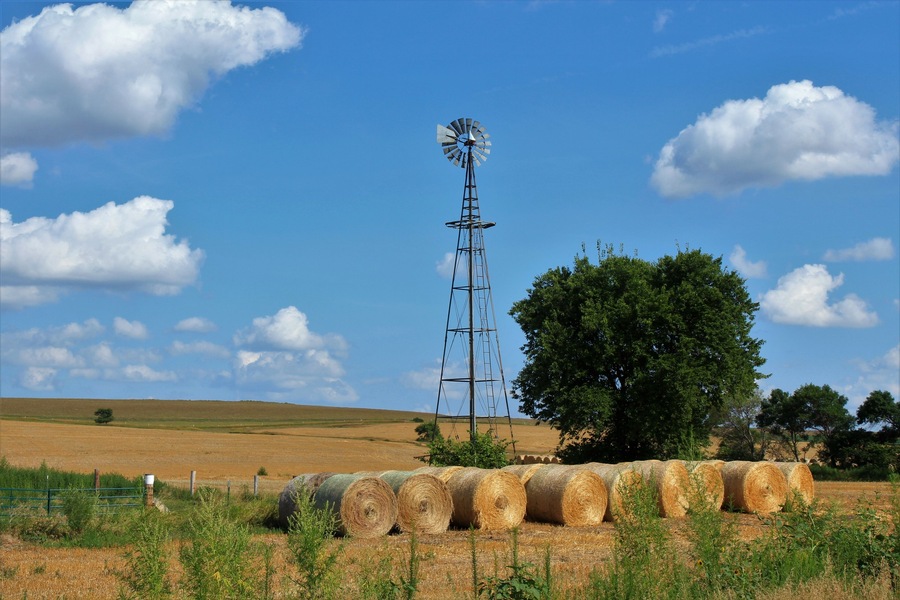 Kansas farm Windmill with hay bales, tree's, blue sky and clouds that's south of Lucas Kansas USA out in the country.