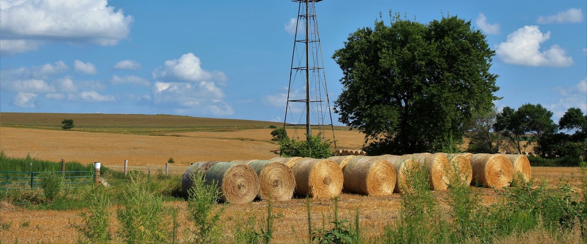 Kansas farm Windmill with hay bales, tree's, blue sky and clouds that's south of Lucas Kansas USA out in the country.