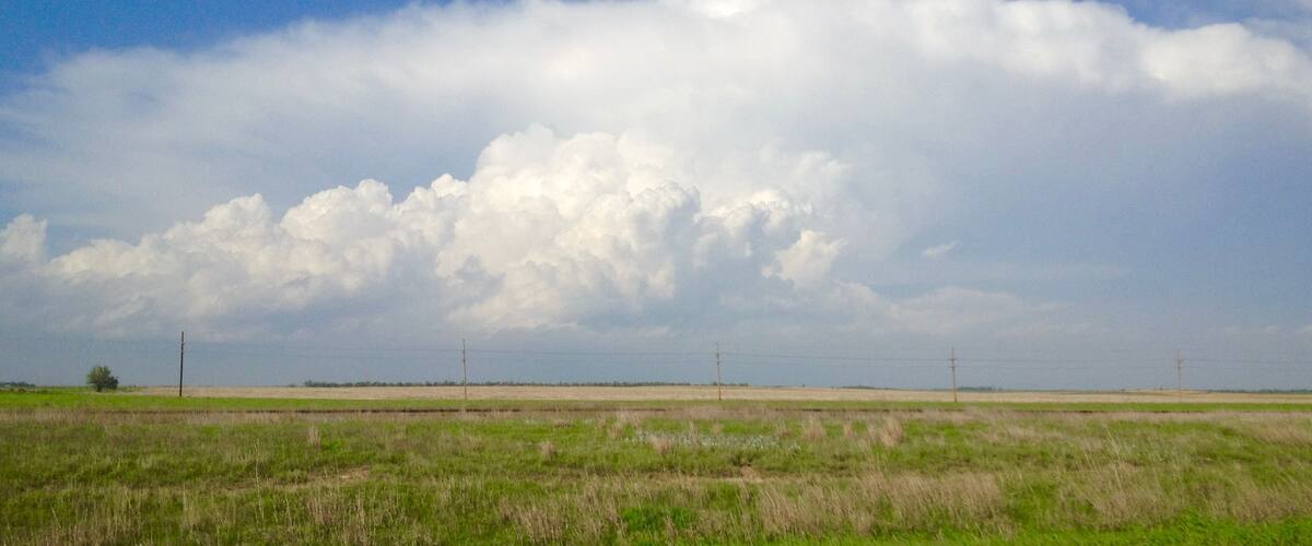 A wide-open field with power lines and a cloudy sky.