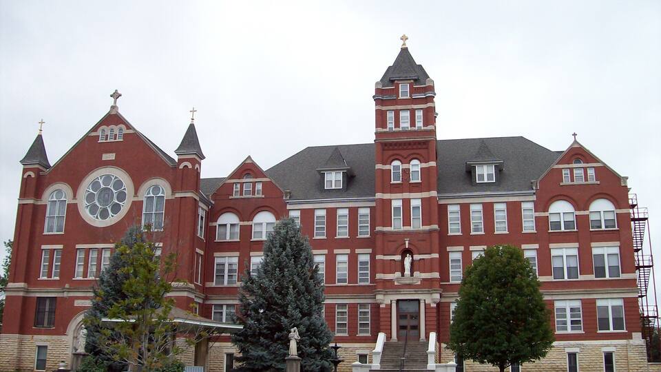A large, historic red brick building with multiple towers and a prominent clock tower.