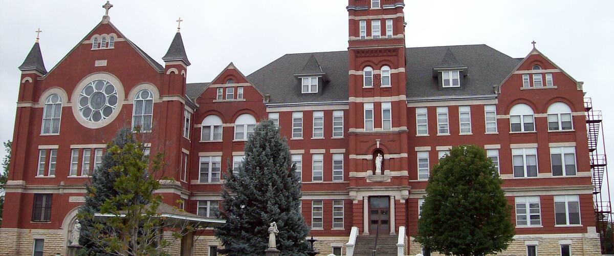 A large, historic red brick building with multiple towers and a prominent clock tower.