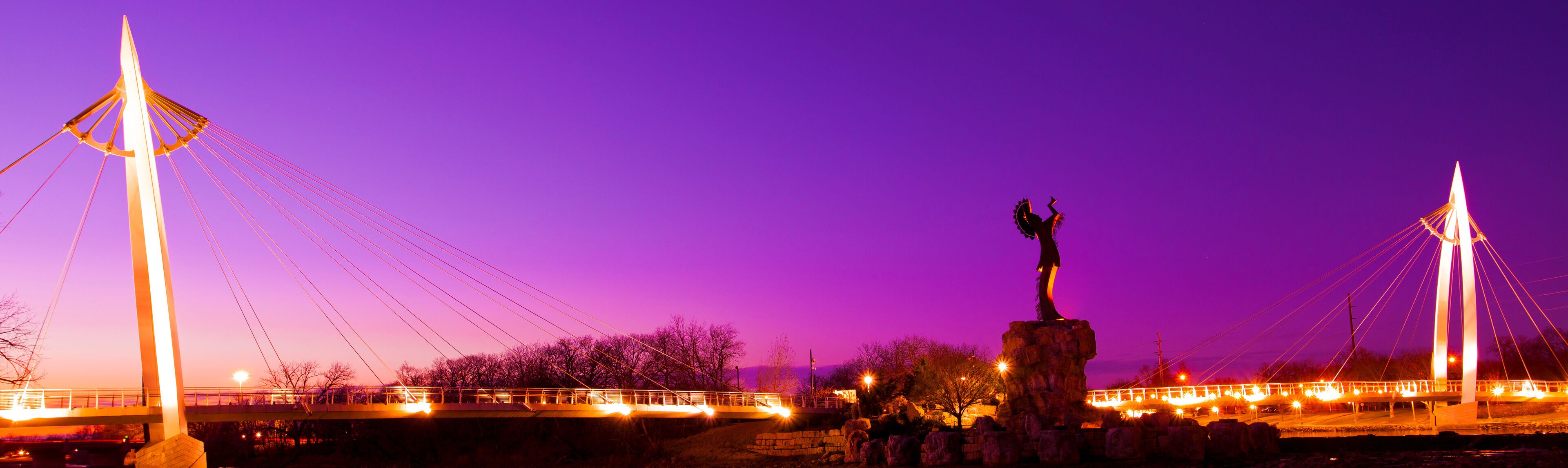 A bridge with a statue in the center, set against a purple sky.