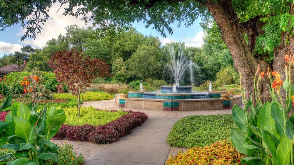 Un jardin agrémenté d’une fontaine, d’une végétation luxuriante et d’une grande variété de fleurs aux couleurs vives.