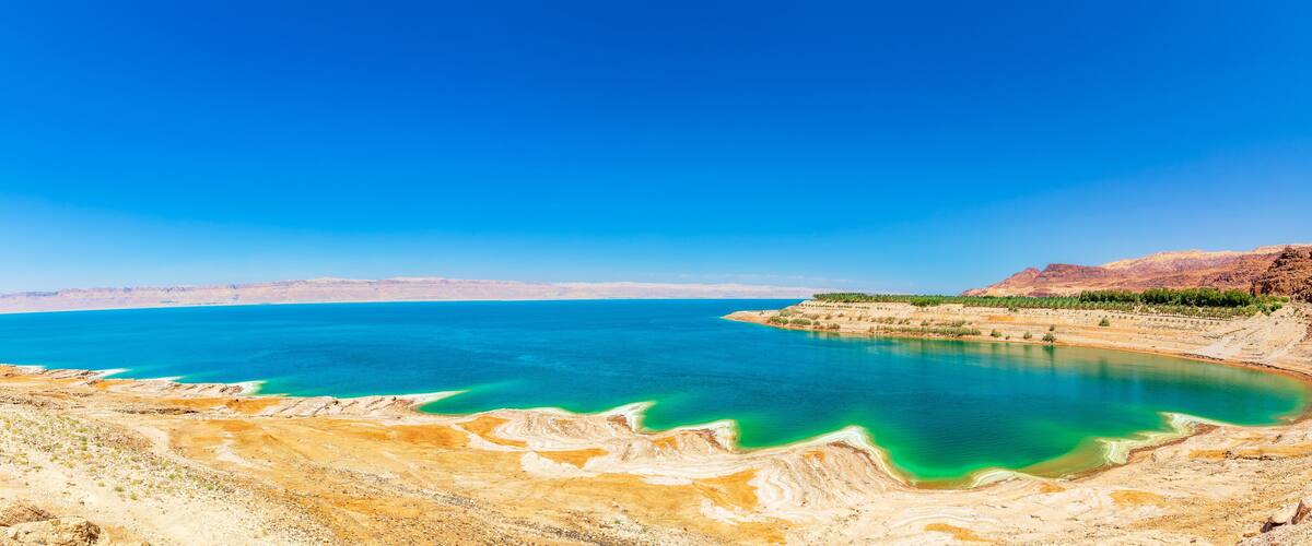 A large body of water with turquoise and green hues, surrounded by arid, rocky terrain and distant mountains.