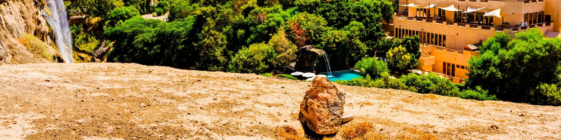 A mountainous landscape with a waterfall, lush greenery, and a modern building complex.
