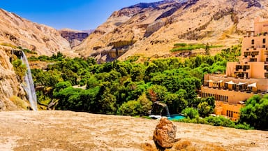 Paisagem montanhosa com cachoeira, vegetação exuberante e um complexo de edifícios modernos.