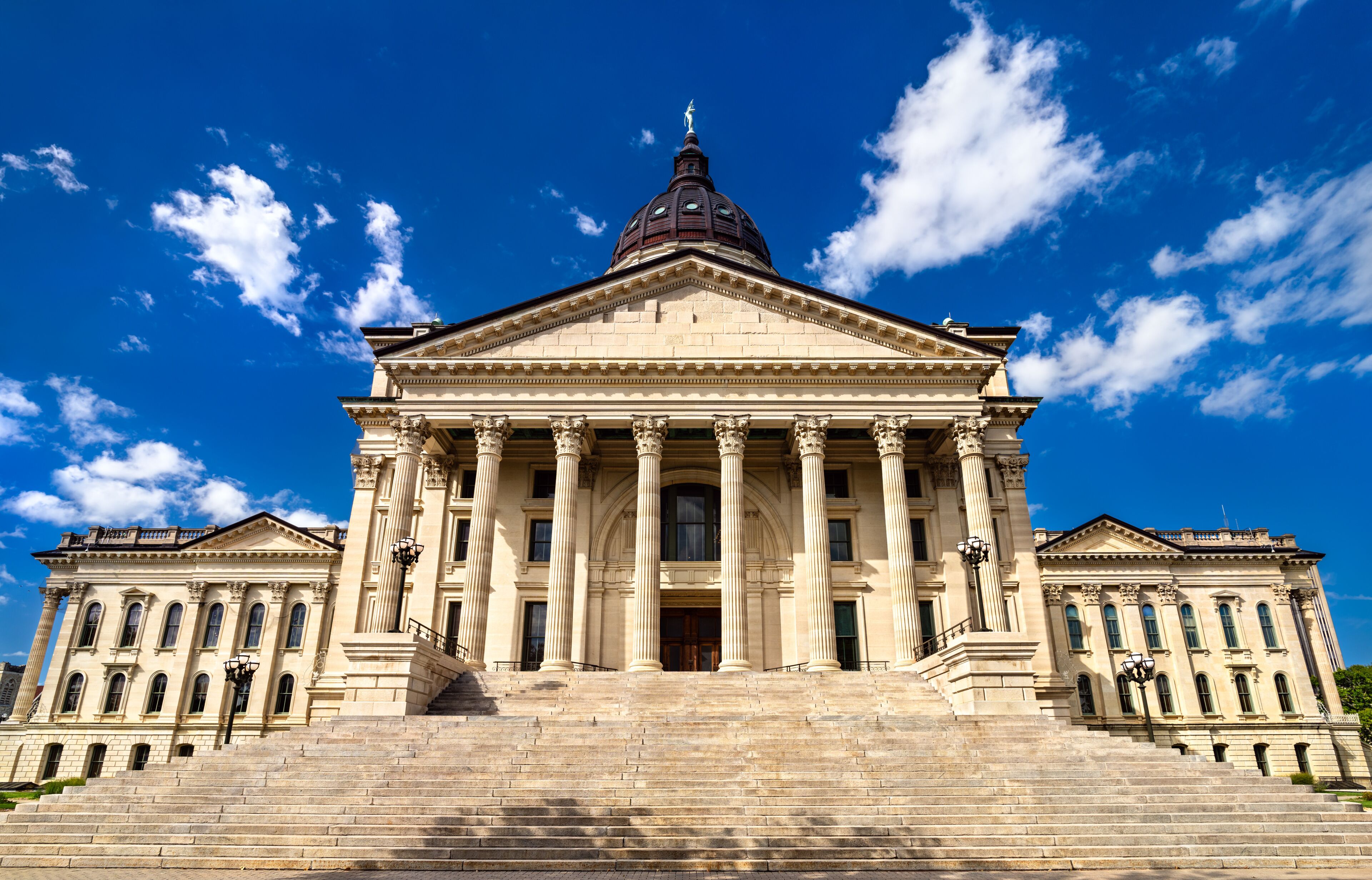 Kansas State Capitol in Topeka. Historic French Renaissance Revival architecture features a limestone facade with columns and a grand staircase under a blue sky