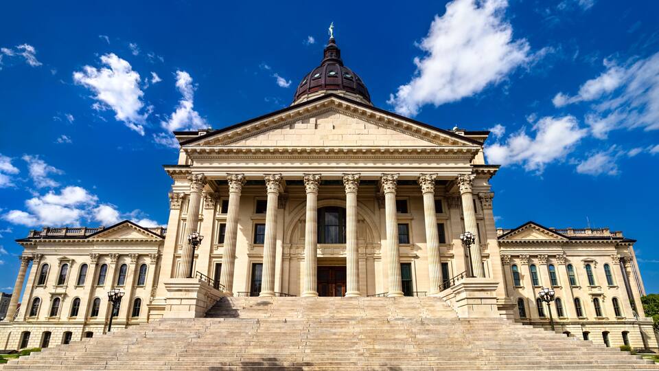 Kansas State Capitol in Topeka. Historic French Renaissance Revival architecture features a limestone facade with columns and a grand staircase under a blue sky