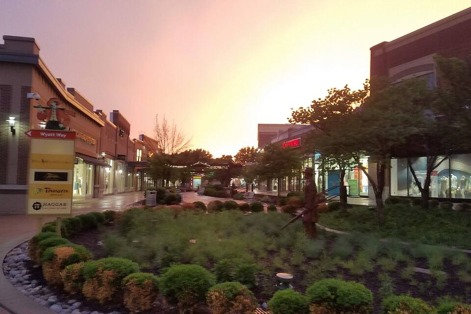 Un espace commercial agrémenté d’un jardin paysager, de boutiques et d’un coucher de soleil en arrière-plan.